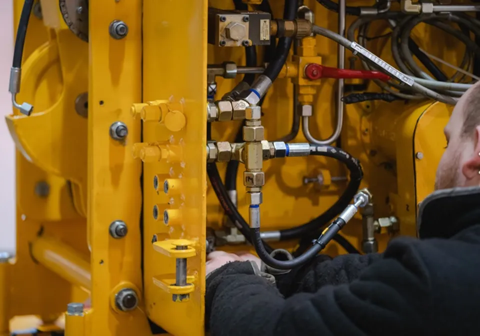 Fagarbeider kobler hydraulikkslanger på en gul anleggsmaskin